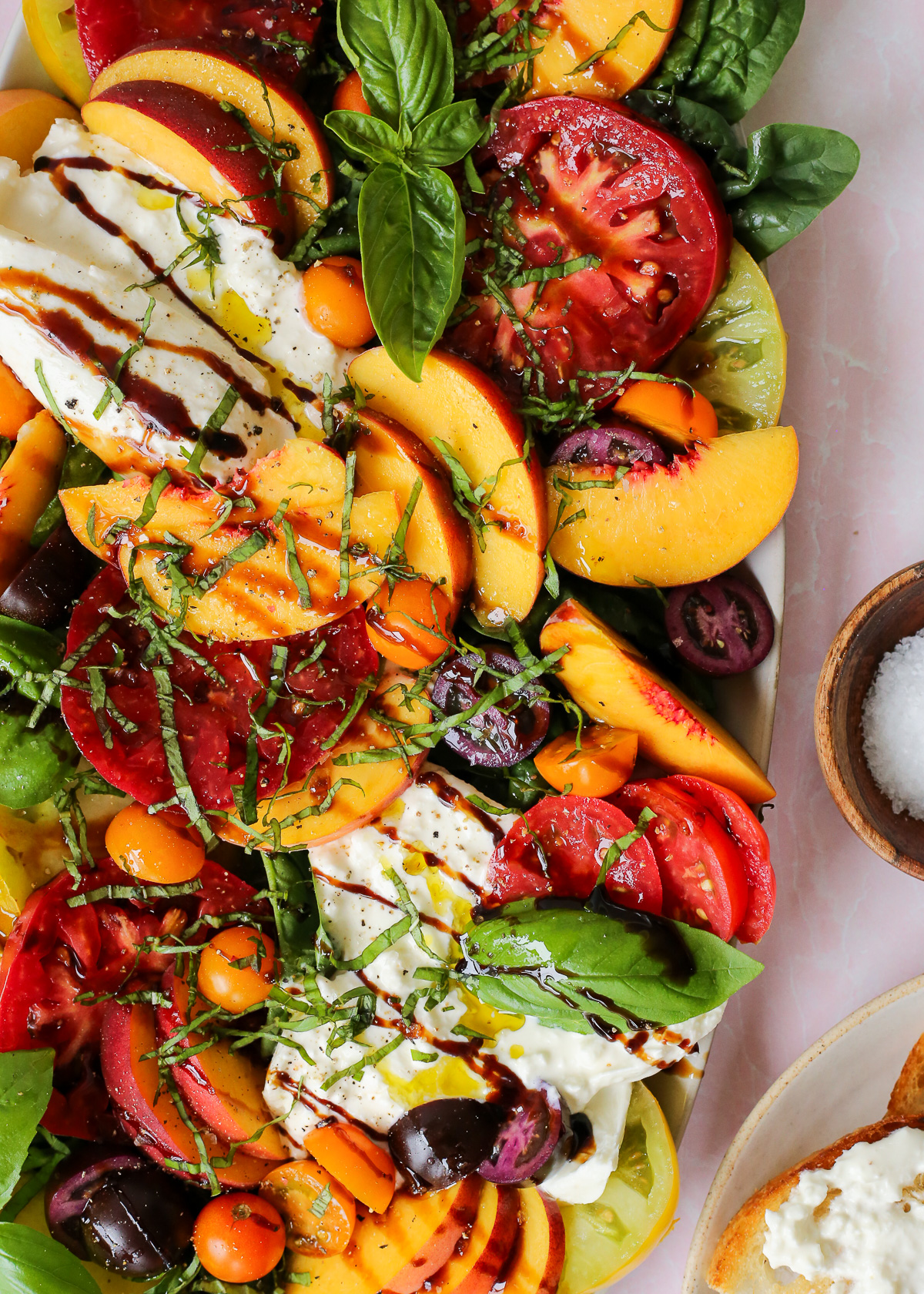 Overhead view of a peach tomato salad, with burrata and fresh basil included, with a light drizzle of olive oil and balsamic glaze on top.