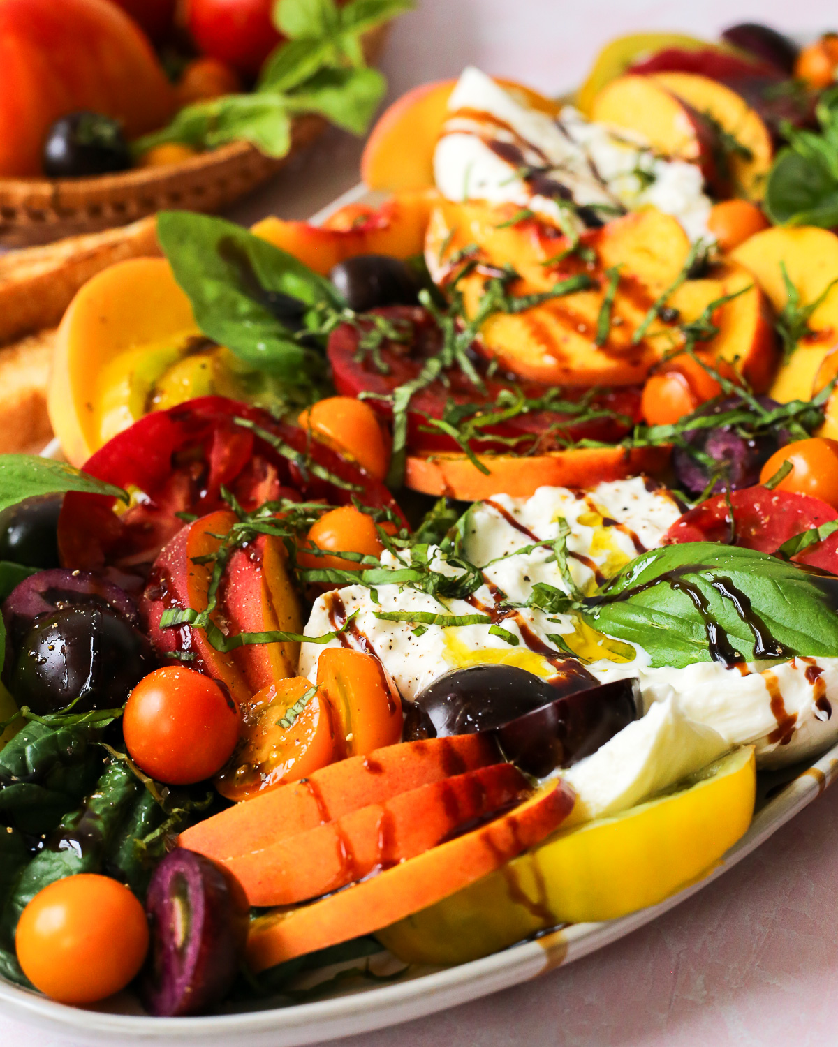A colorful summer salad made with fresh peaches, sliced tomatoes, burrata cheese, and basil leaves topped with a drizzle of balsamic glaze.