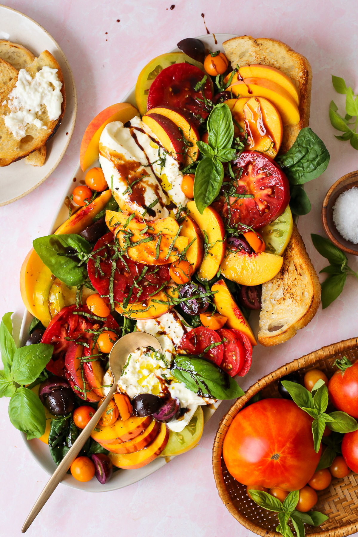 Overhead view of a large summer salad made with peaches, tomatoes, burrata, and basil, served on a kitchen countertop and drizzled with balsamic glaze.