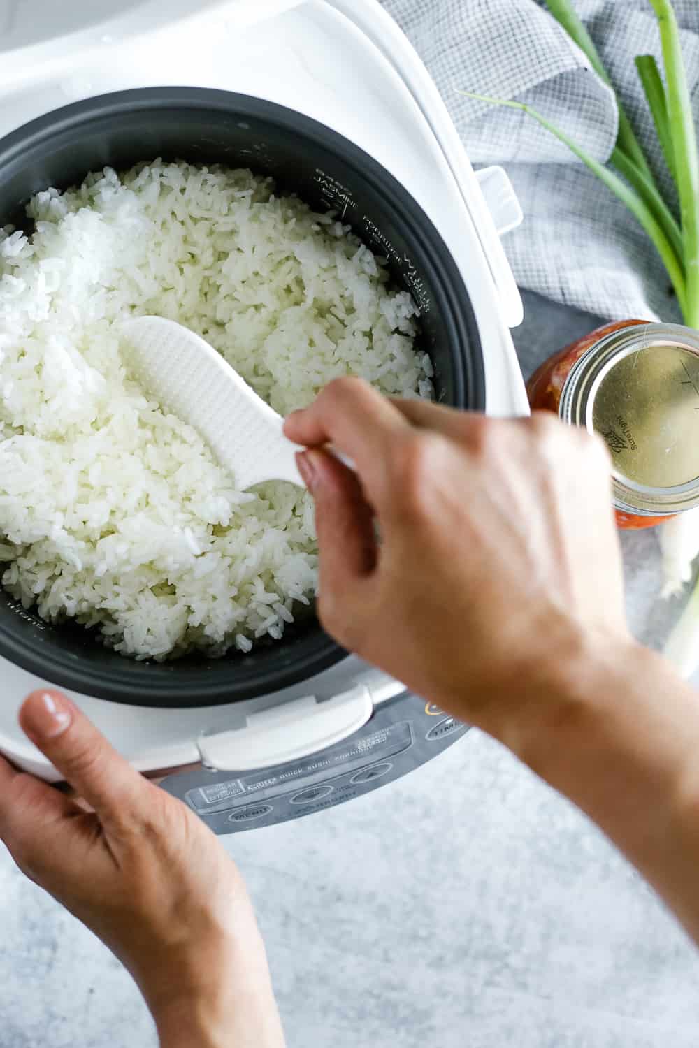 Overhead view of a rice cooker with cooked white rice being stirred 