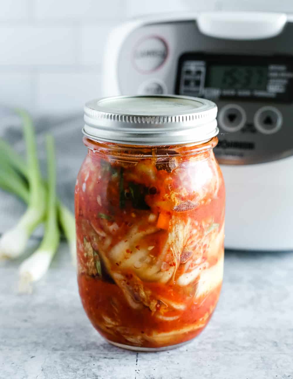 Glass jar of homemade kimchi on kitchen counter in front of a rice cooker