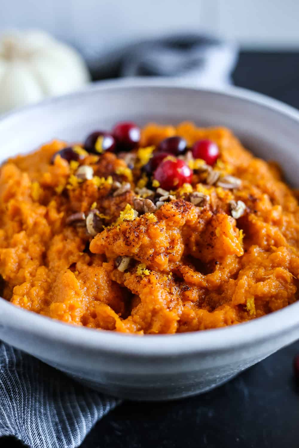Mashed sweet potatoes in a blue ceramic serving bowl, garnished with chopped pecans, orange zest, and fresh cranberries