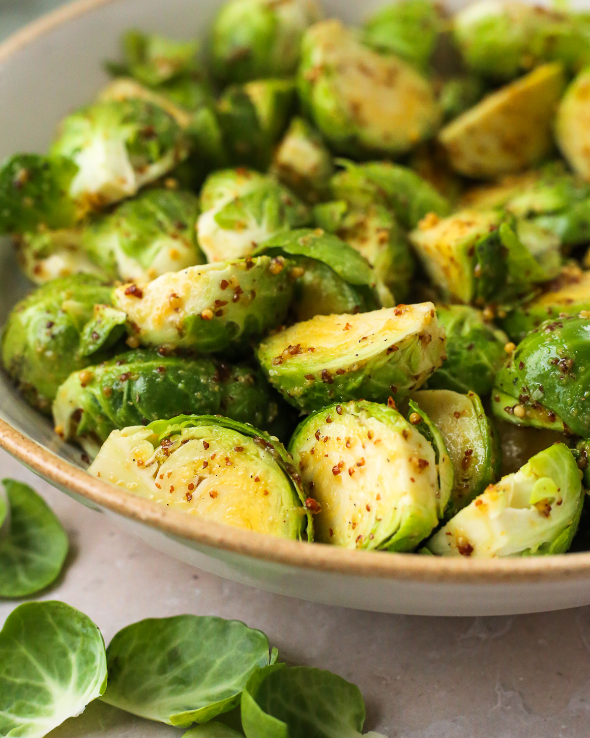 A mixing bowl filled with uncooked Brussels sprouts that have been tossed with whole grain mustard. 