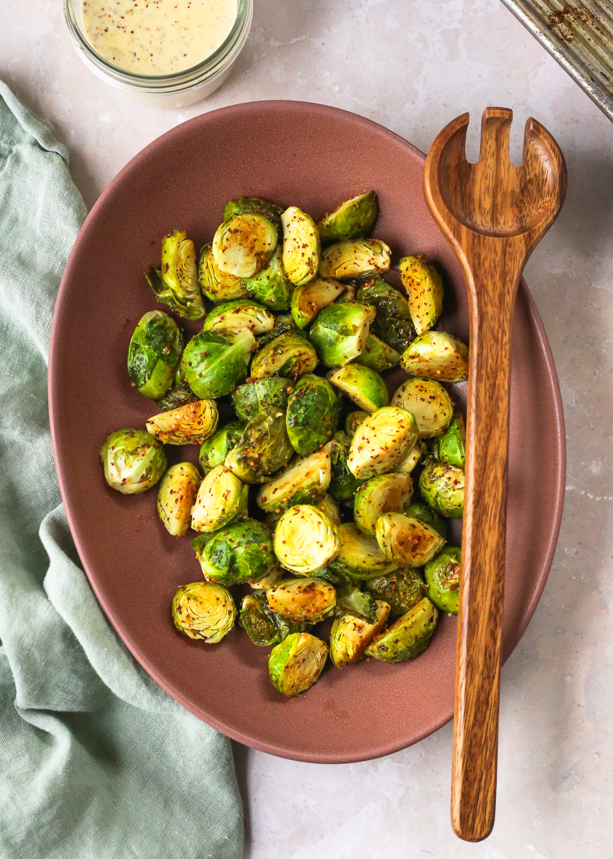 A large ceramic serving dish filled with roasted Brussels sprouts coated in a maple mustard glaze. 