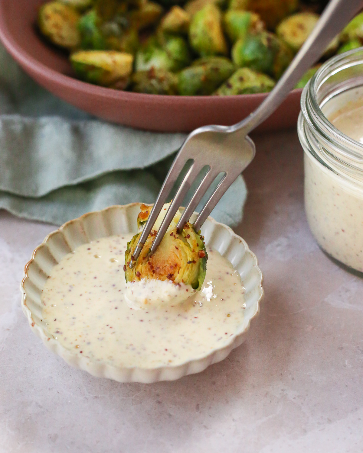 A fork dipping a roasted Brussels sprout into a creamy dijon aioli sauce. 