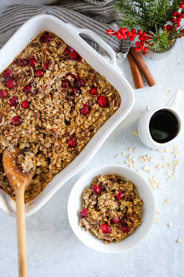 Maple Pecan Baked Oatmeal in a white baking dish and single serving in a white bowl, with seasonal holiday decorations on a kitchen countertop