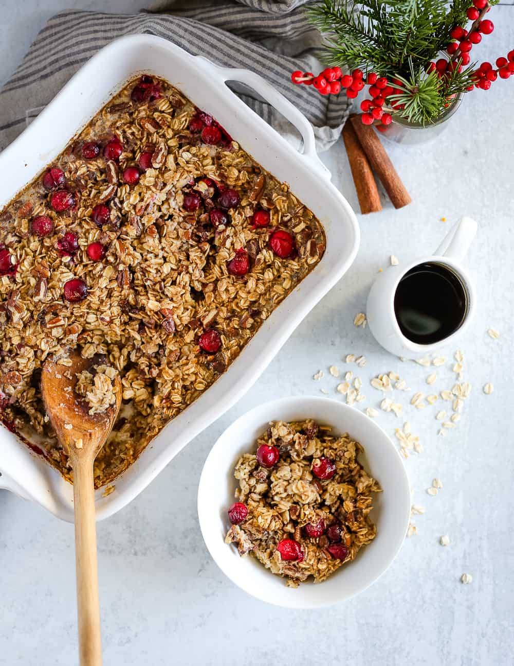 Maple Pecan Baked Oatmeal in a white baking dish and single serving in a white bowl, with seasonal holiday decorations on a kitchen countertop