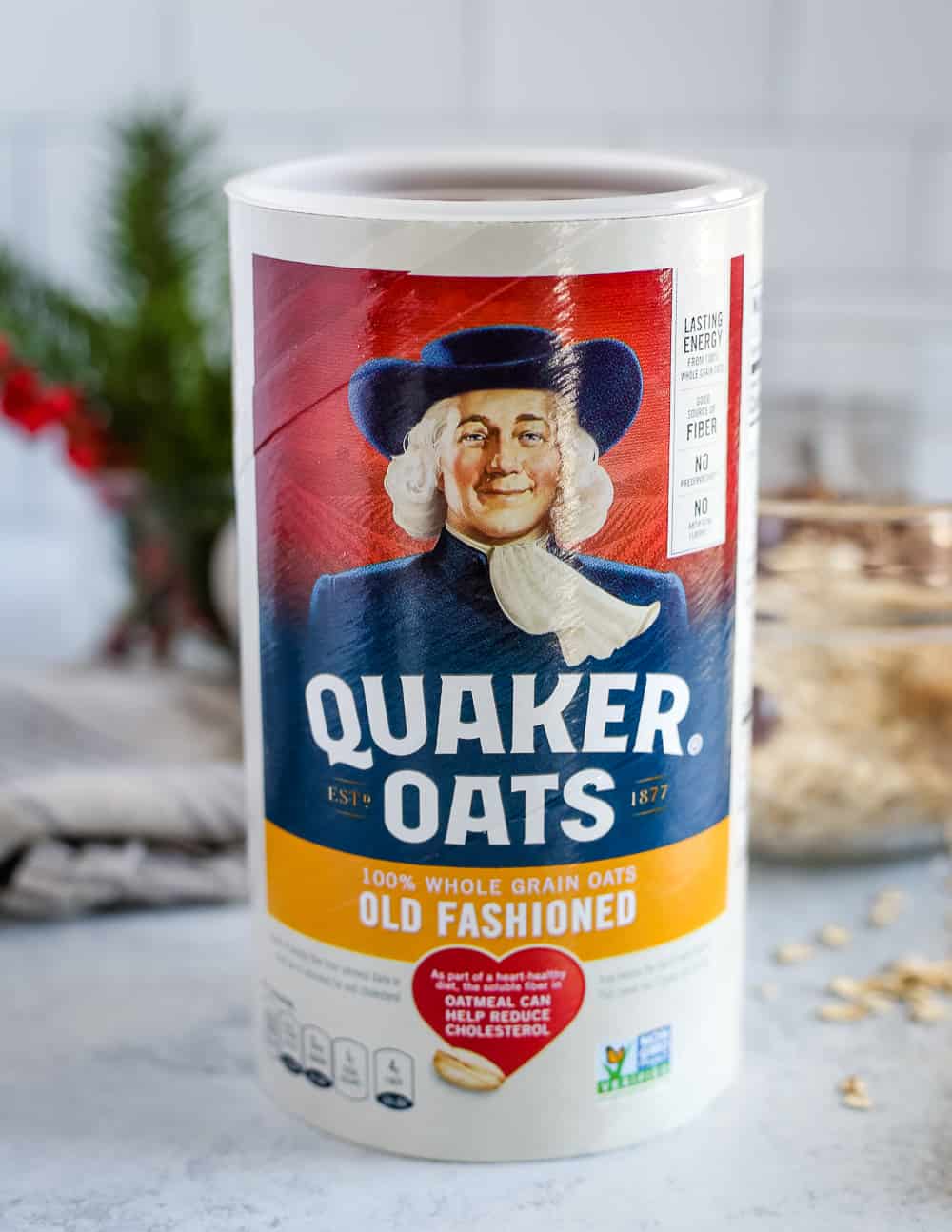 A colorful canister of Quaker Old Fashioned Oats on a kitchen counter with seasonal holiday decorations in the background