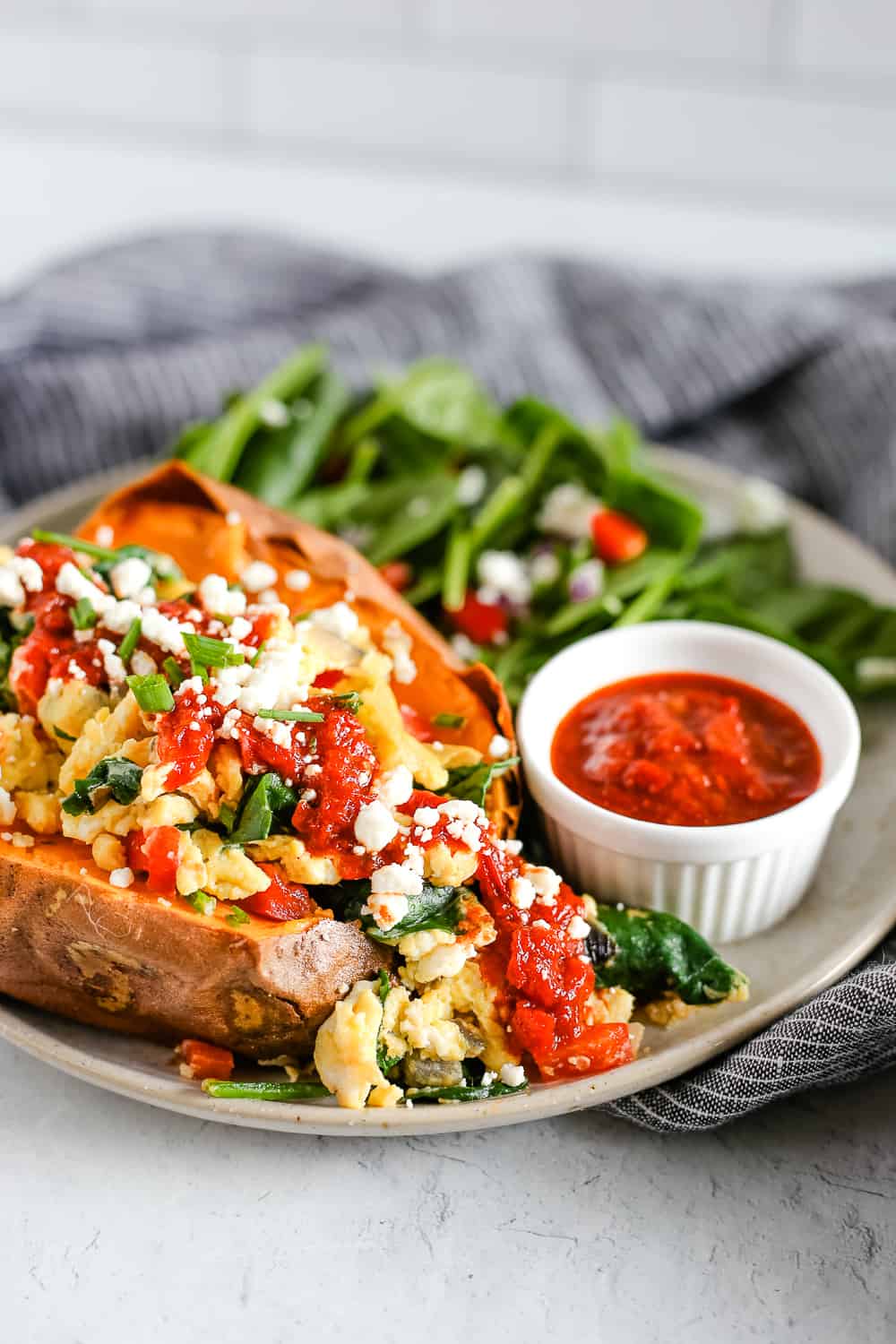 A plate with a breakfast stuffed sweet potato, topped with scrambled eggs and veggies, served with a side salad