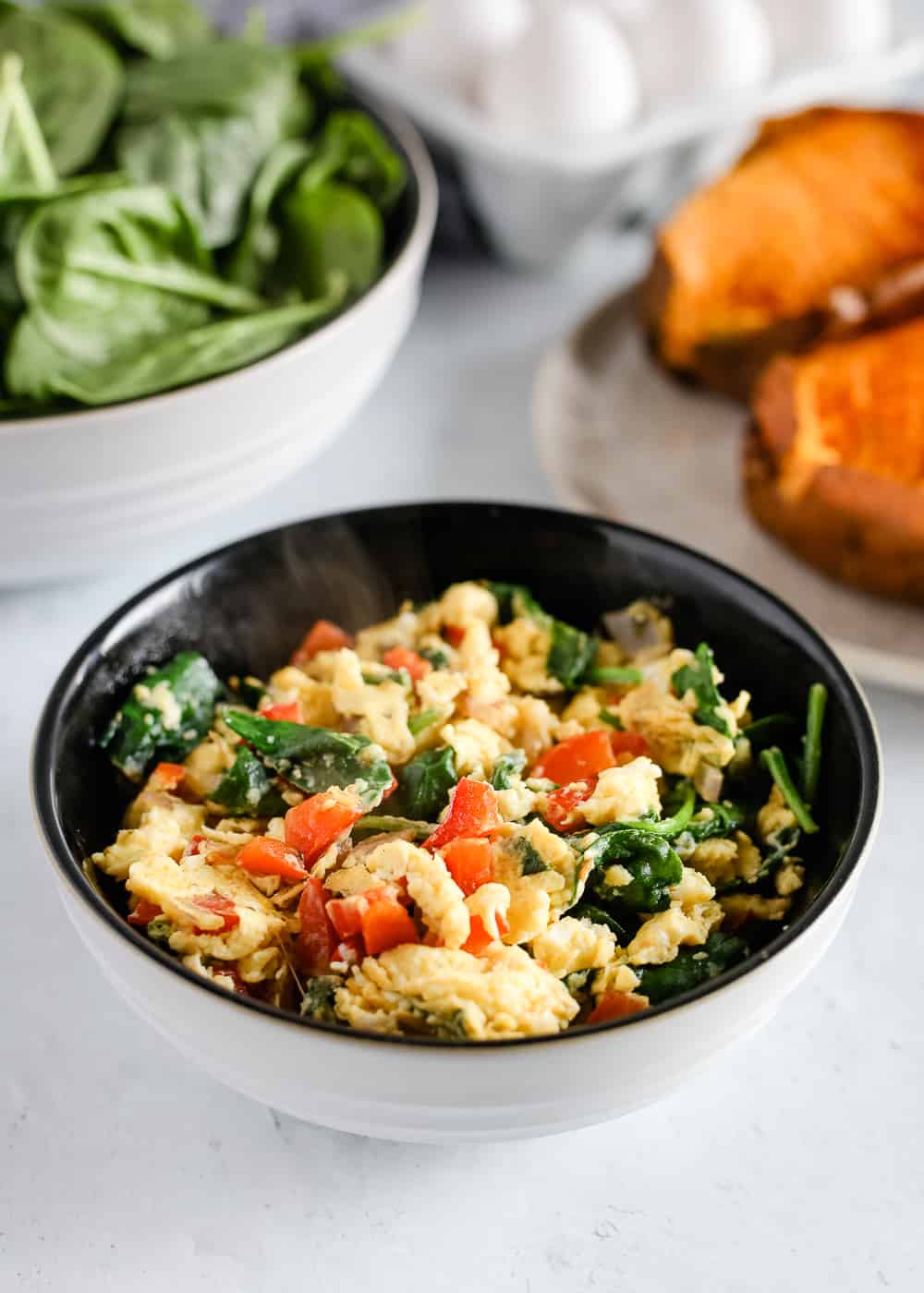 A serving bowl with scrambled eggs and veggies on a white kitchen counter