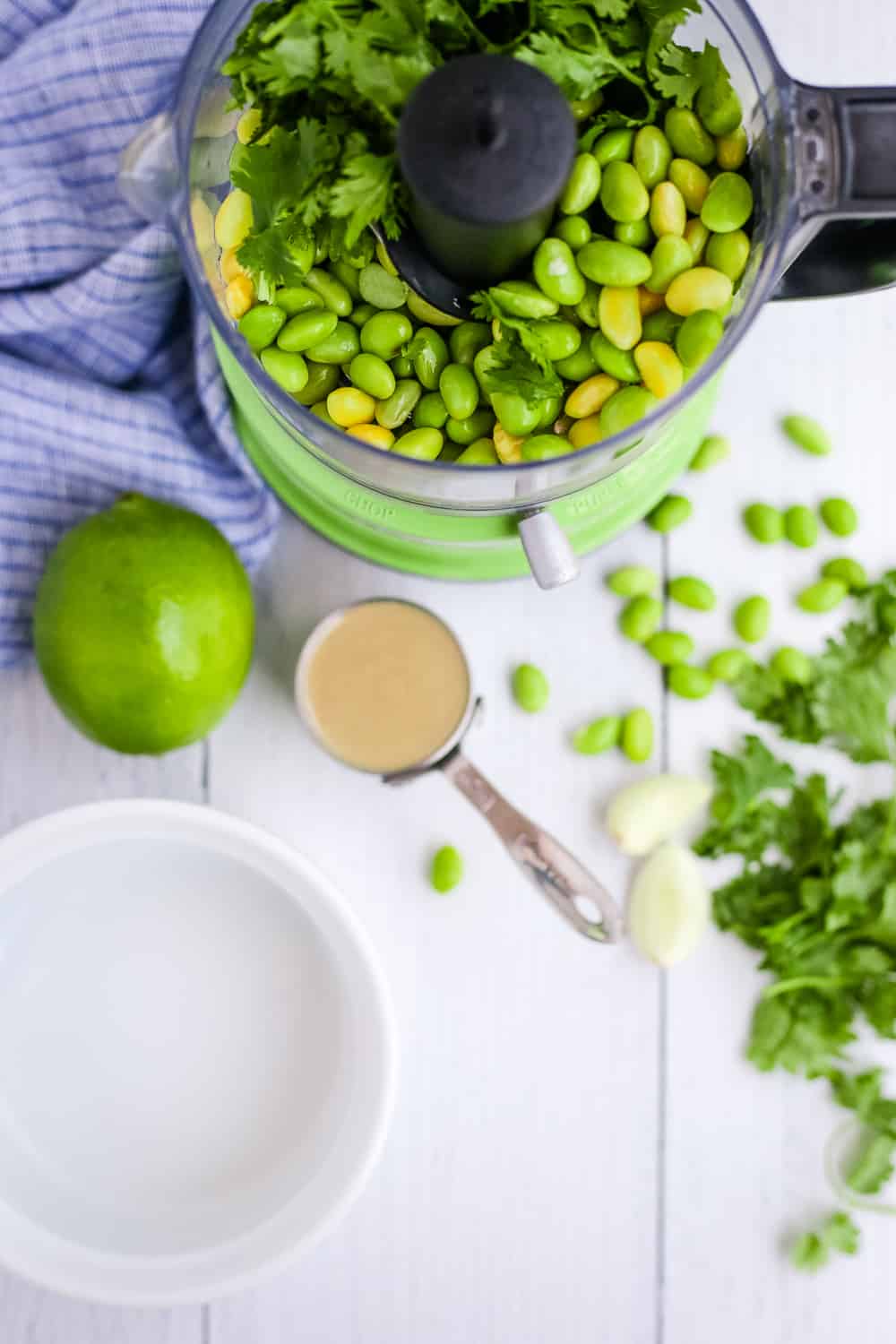 A food processor with shelled edamame and other ingredients to make homemade hummus