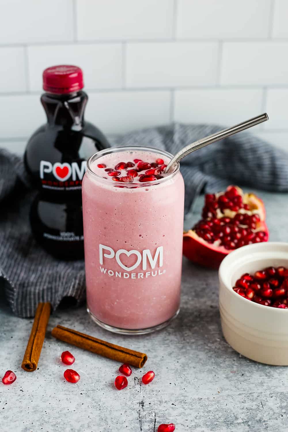 A bright pink Spiced Pomegranate Smoothie sits on a kitchen countertop with a fresh pomegranate and bottle of pomegranate juice