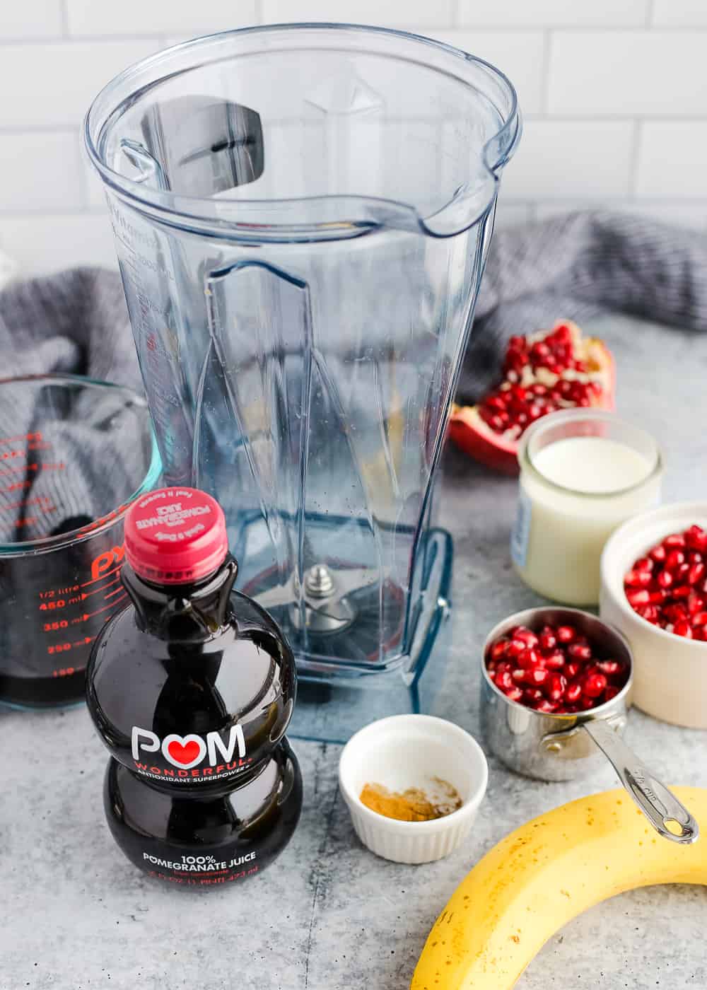 The ingredients and blender for a Spiced Pomegranate Smoothie are on a kitchen counter