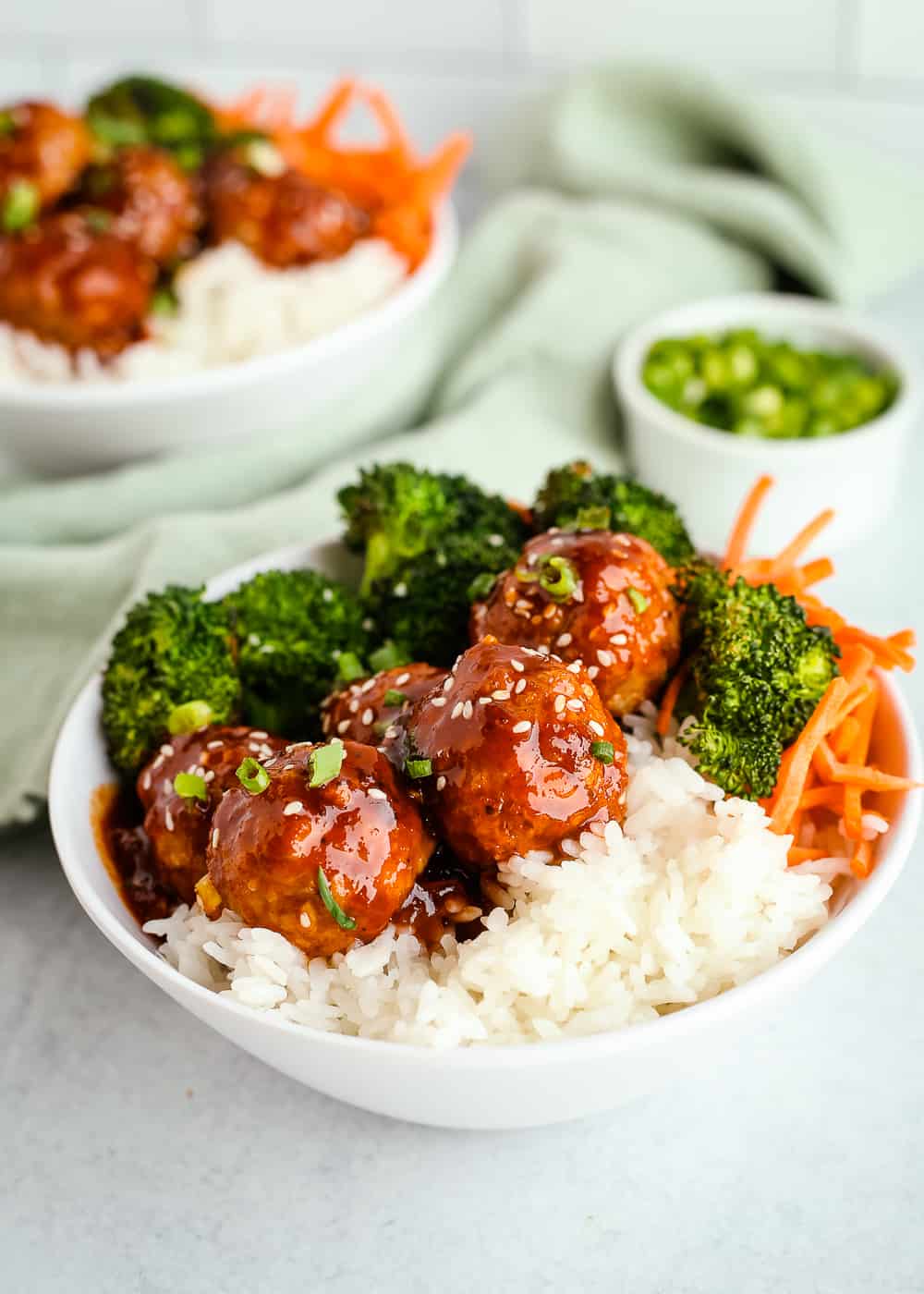 Two white bowls filled with white rice, roasted broccoli, and sweet and spicy turkey meatballs on a kitchen counter