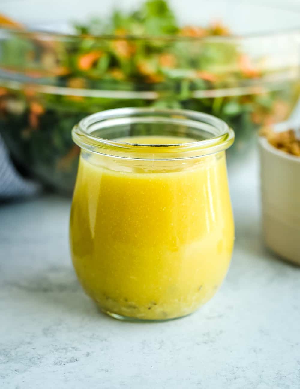 A small glass jar filled with a homemade Lemon-Garlic Dressing to be served with this Israeli couscous recipe