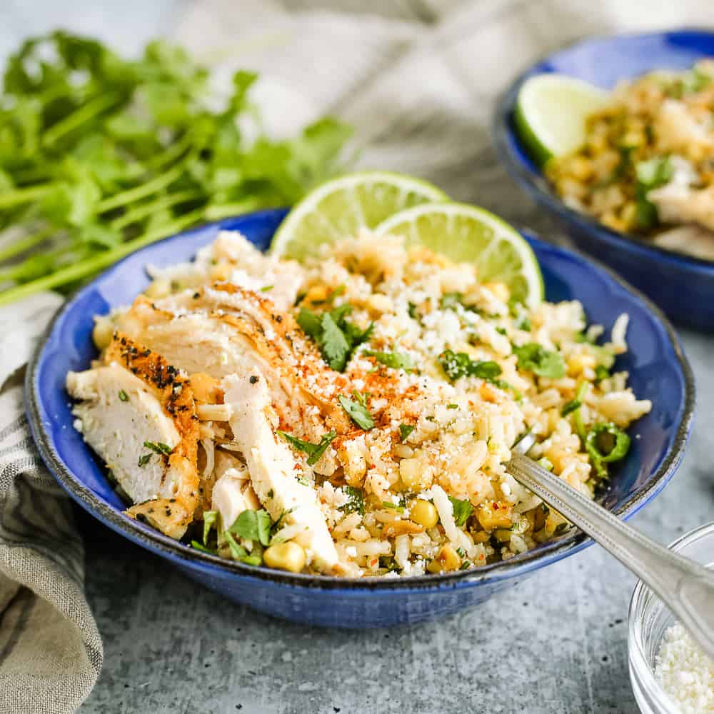 Mexican Street Corn and rice bowls, esquites inspired, topped with chicken and lime wedges in a bright blue ceramic bowl on a kitchen counter