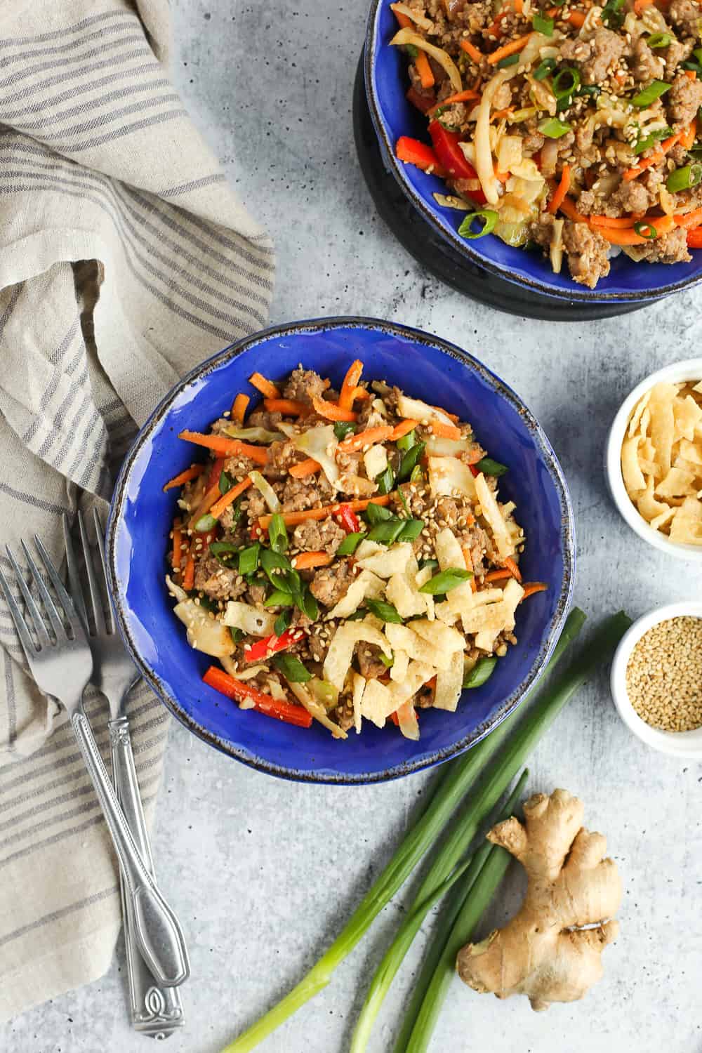 Overhead view of two bright blue bowls filled with ground pork, rice, and colorful veggies and garnished on a kitchen countertop