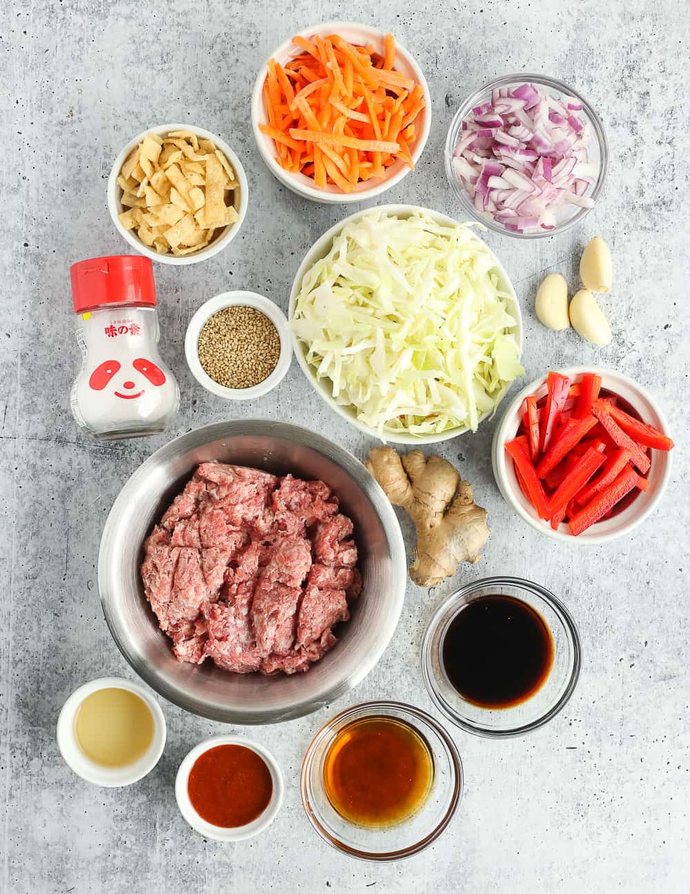 Overhead view for all the ingredients of a ground pork egg roll in a bowl recipe on a kitchen countertop in clear glass ramekins and silver prep bowls