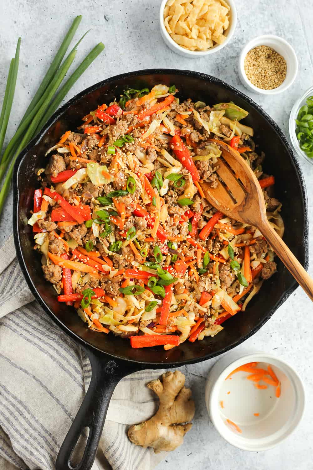 A black cast iron skillet filled with ground pork, colorful veggies, and topped with sliced green onions