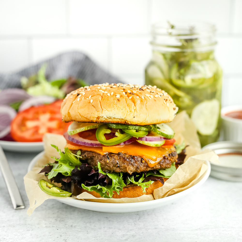 Side view of a classic beef burger with a toasted bun, lettuce, tomatoes, onions, and pickles