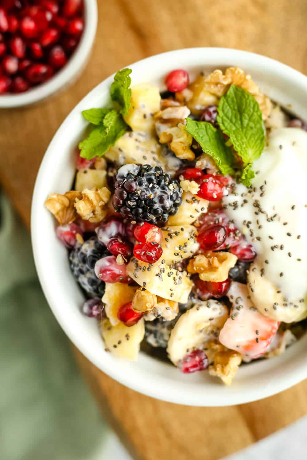 A closeup overhead shot of a bowl of creamy fruit salad with yogurt and colorful fruit on a wooden serving tray