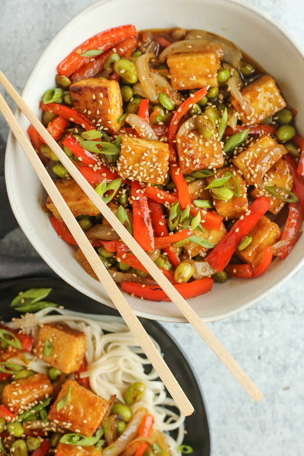An overhead view of a vegetarian orange tofu stir fry recipe in a white bowl with wooden chopsticks