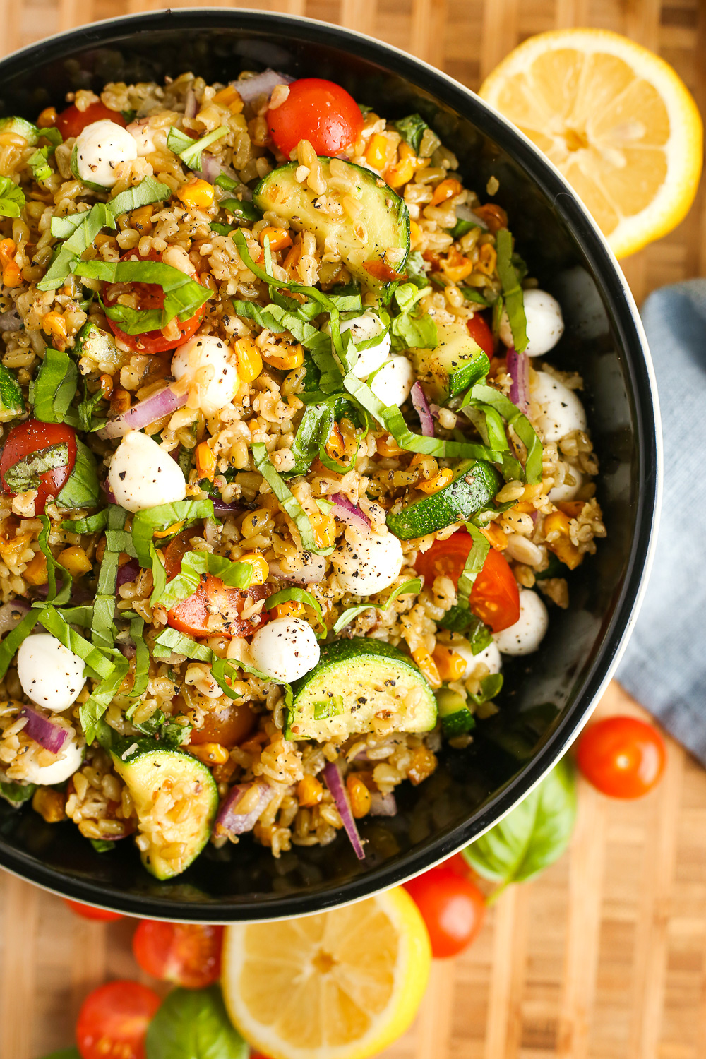 Overhead view of a summer salad with grains, tomatoes, mozzarella, zucchini, corn, and chopped basil on a butcher block countertop