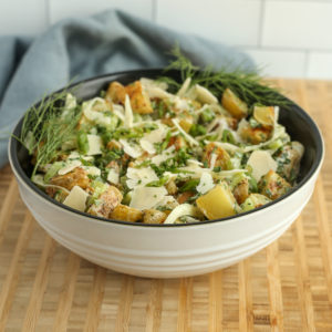 Side view of a bowl of creamy greek yogurt potato salad with herbs on a butcher block counter top