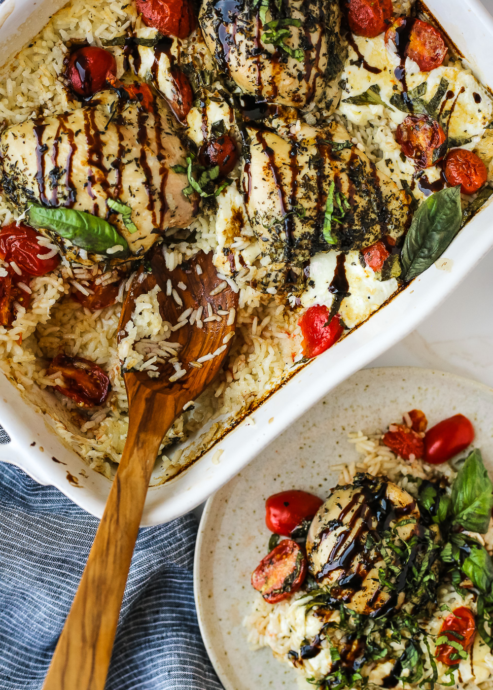 Overhead view of a single serving of Caprese Chicken and Rice Bake on a plate next to the casserole dish that holds the rest of the recipe of baked chicken and rice