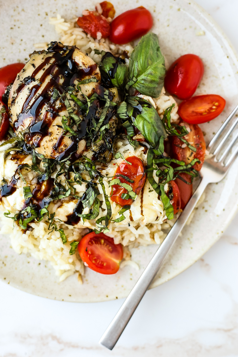 Overhead view of a baked caprese chicken dish served with rice and sliced tomatoes and basil