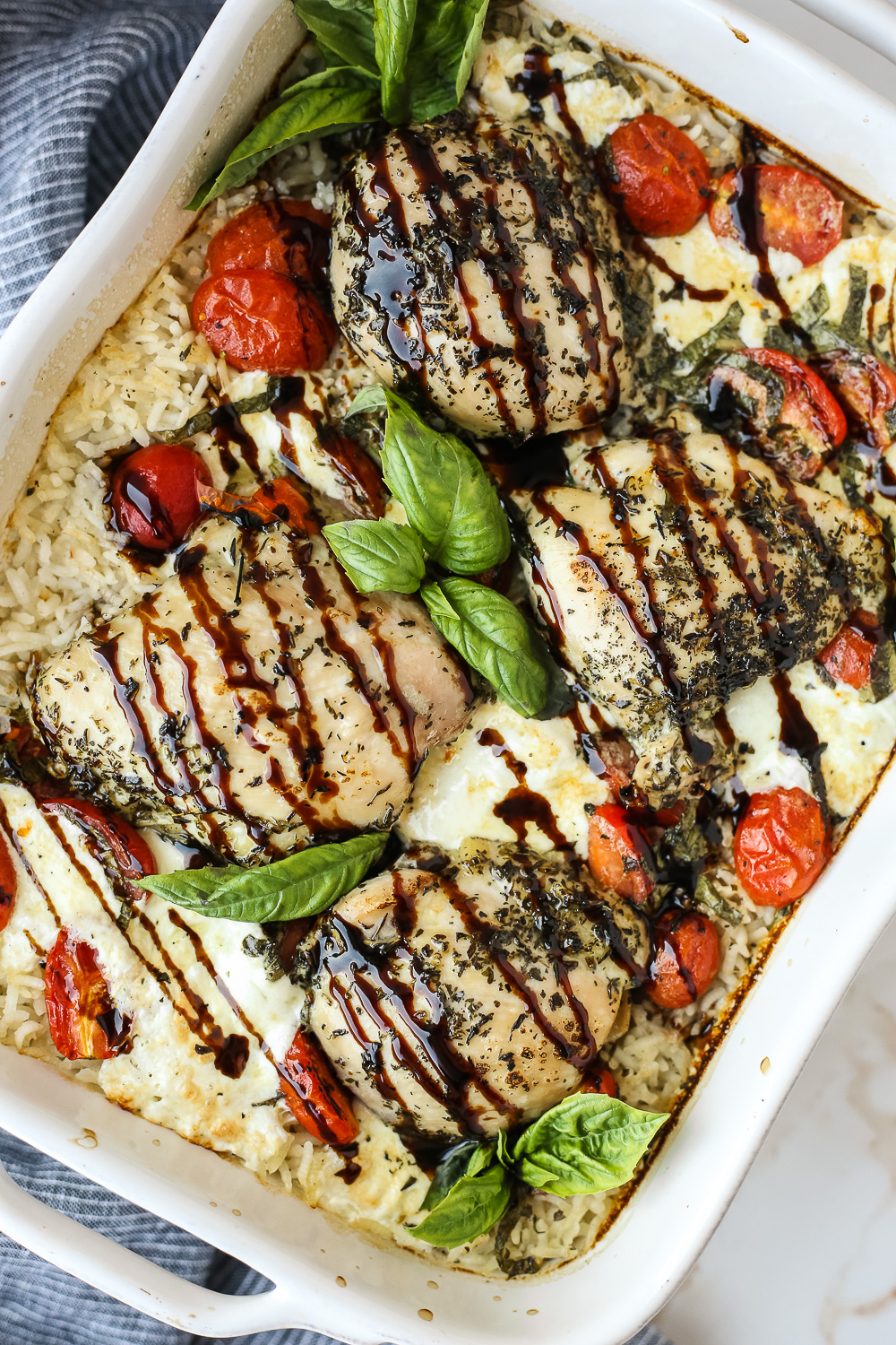 overhead view of baked caprese chicken in a white casserole dish with rice, tomatoes, mozzarella cheese, and basil