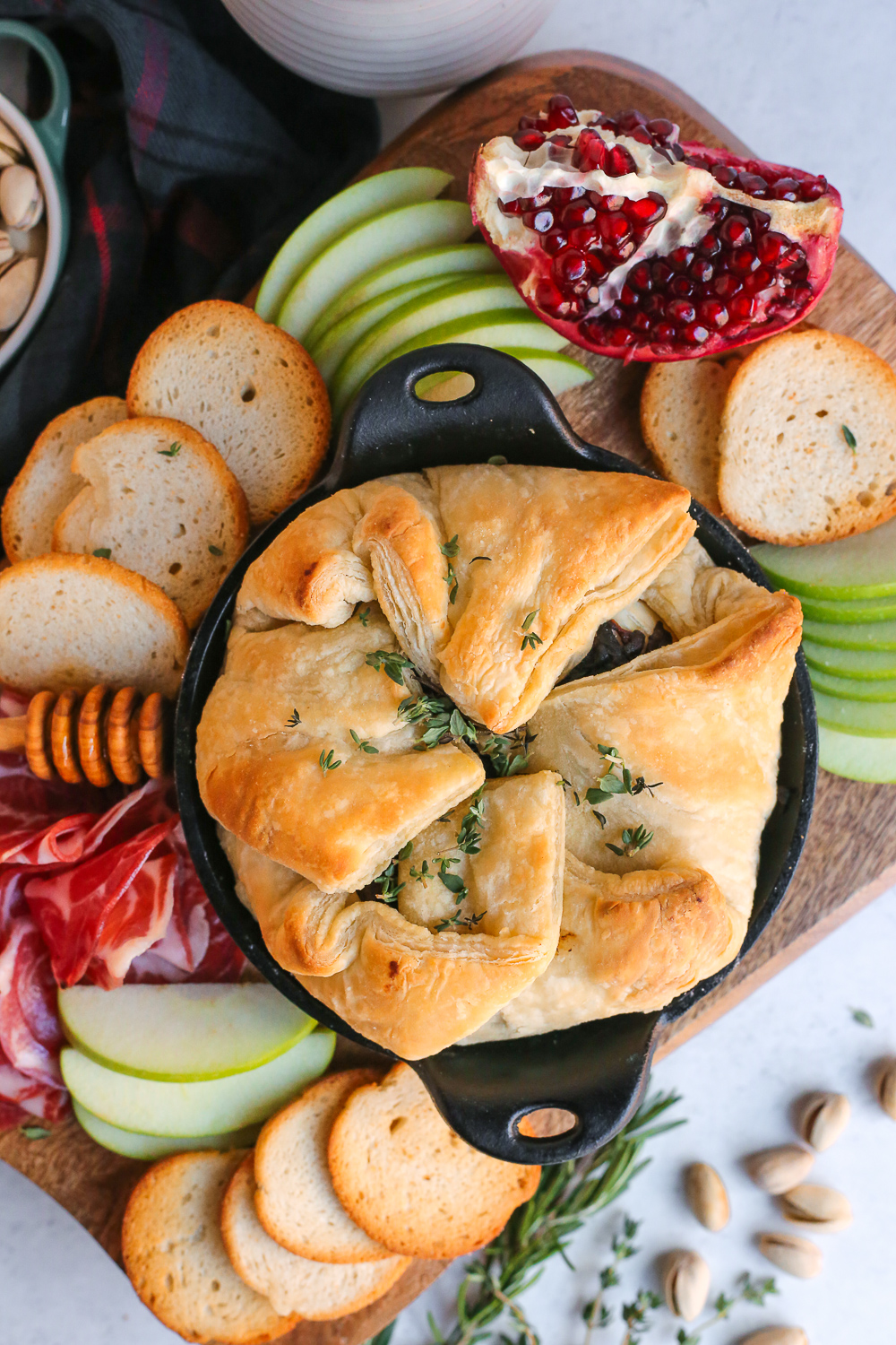 Overhead view of a savory baked brie appetizer in puff pastry on a charcuterie board, garnished with fresh herbs