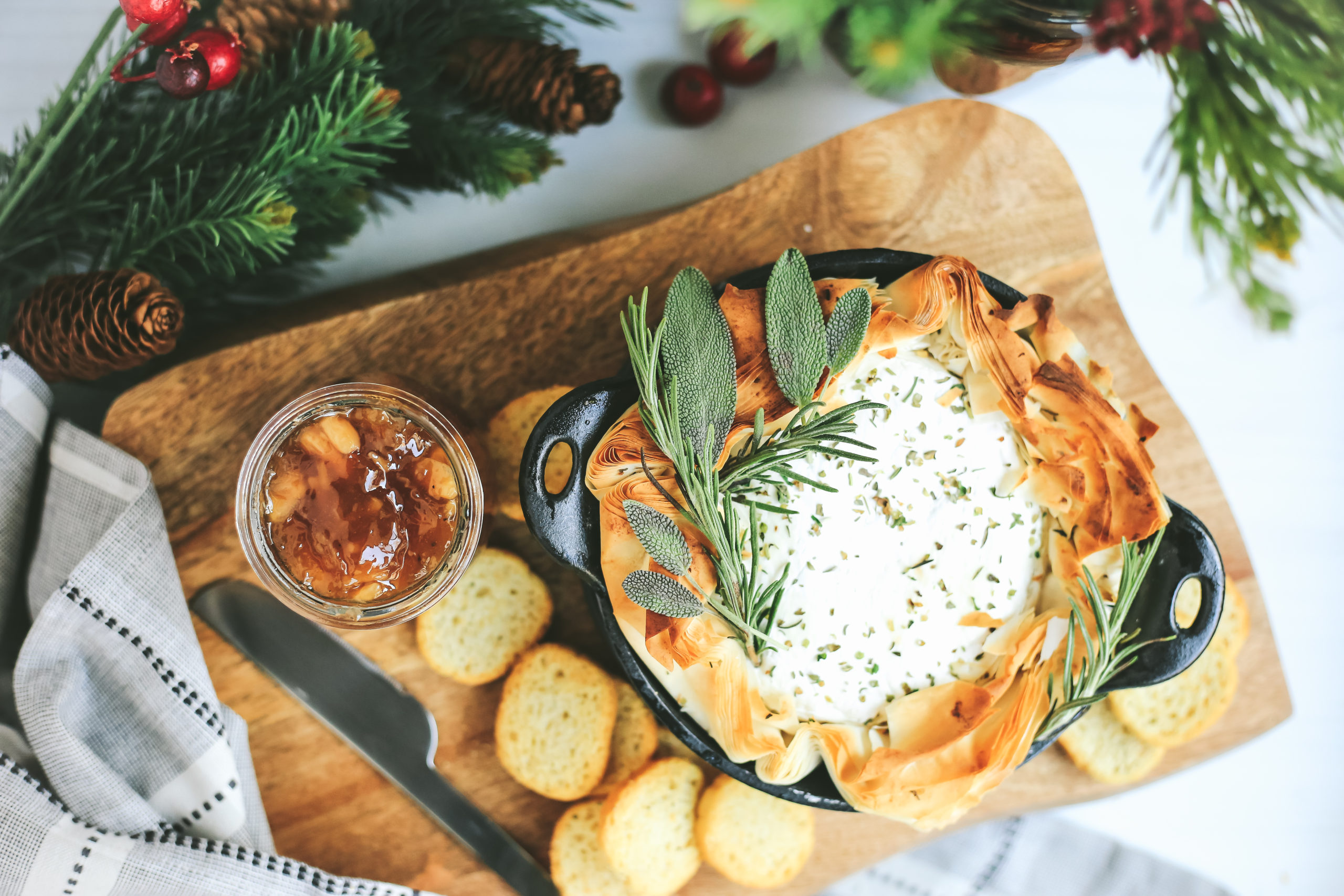 Baked Brie in phyllo dough with herbs, peach jam, and seasonal decorations, served on a wooden platter