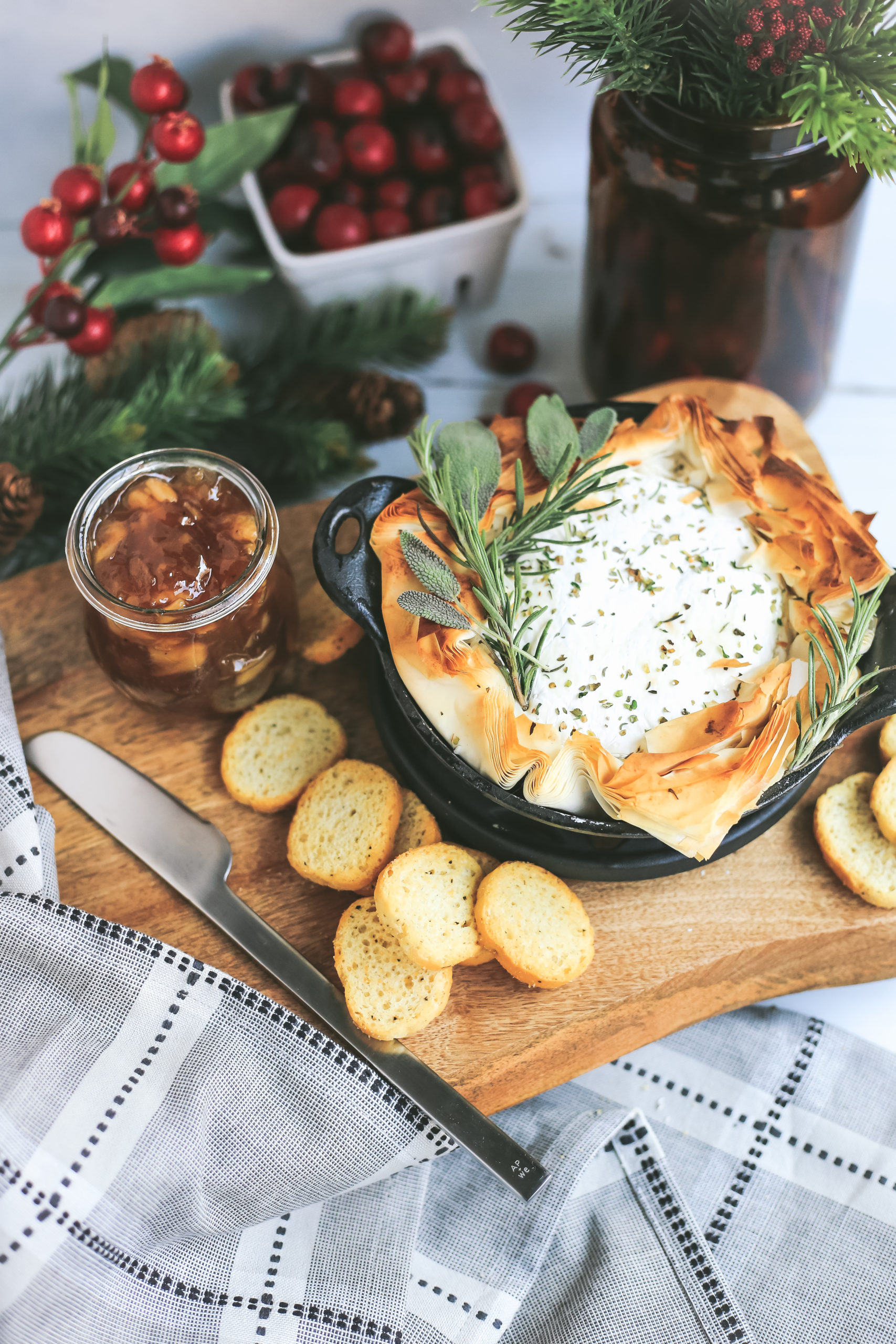 Easy Baked Brie in phyllo dough with savory herbs, peach jam, and seasonal winter decor, served in a small cast iron skillet
