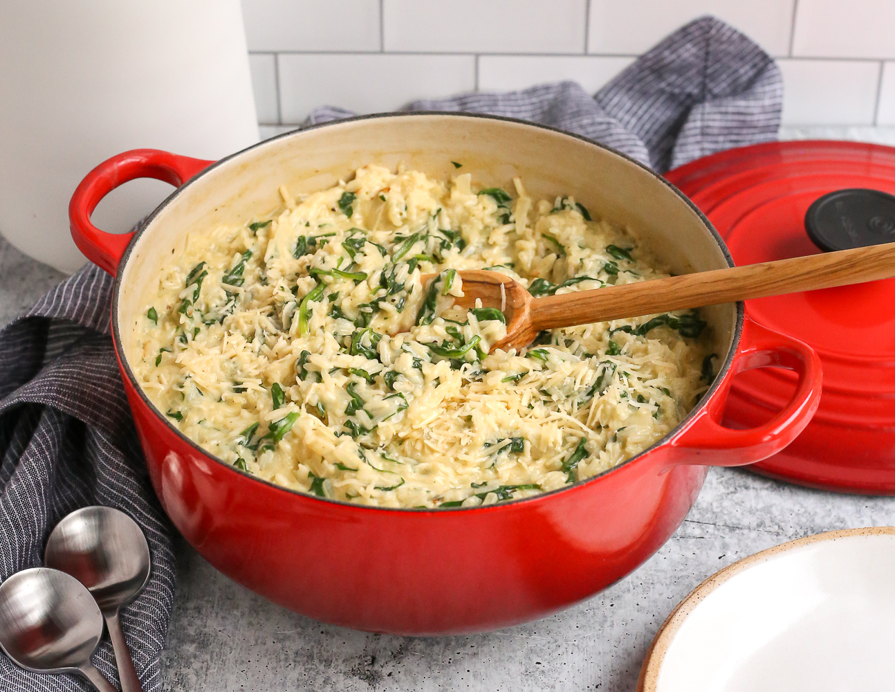 Creamy Spinach Rice in a red dutch oven with a wooden serving spoon, topped with parmesan cheese