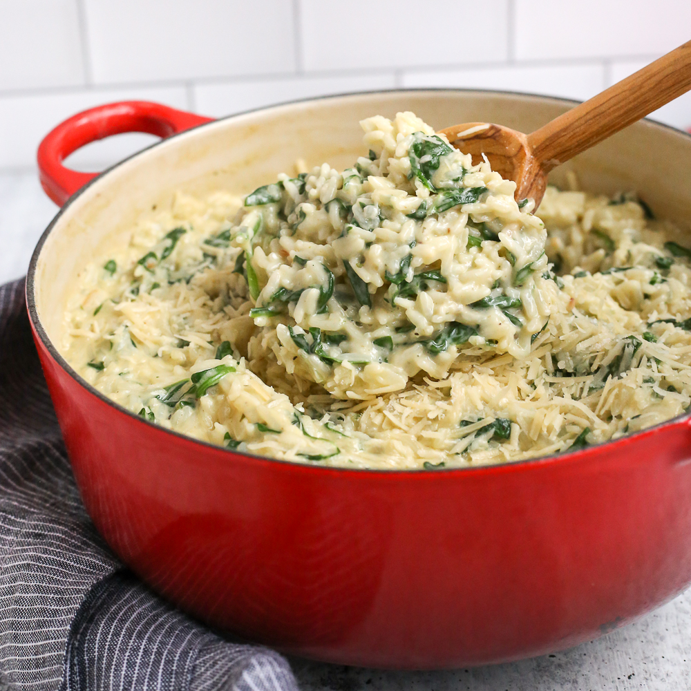 A wooden spoon lifts a scoop of creamy spinach rice from a red dutch oven to serve as an easy rice side dish