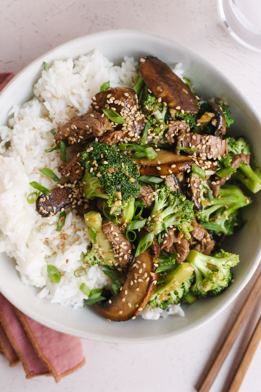 Overhead view of a sauce-covered beef and broccoli stir fry on top of white rice, garnished with green onions and sesame seeds