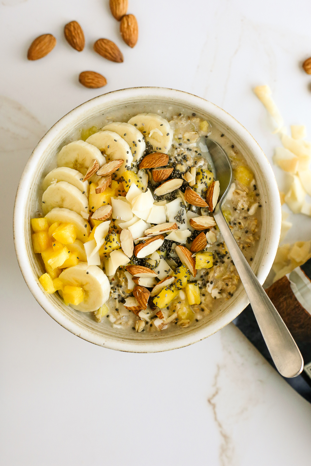 Bowl of pineapple banana protein oats with toasted coconut, almonds, and chia seeds