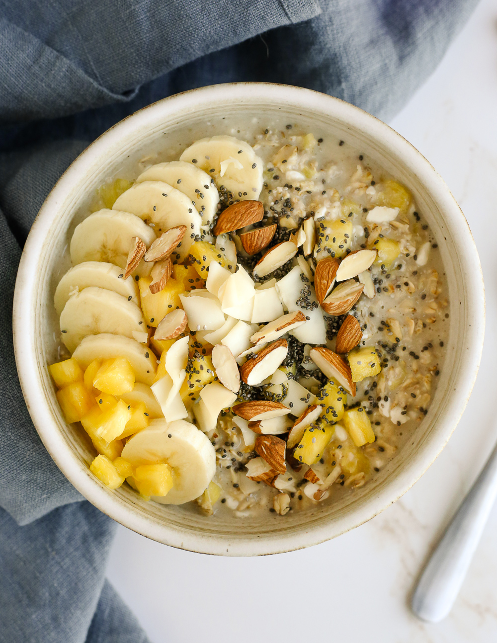 A bowl of pineapple banana protein oats, topped with toasted coconut, sliced almonds, and chia seeds