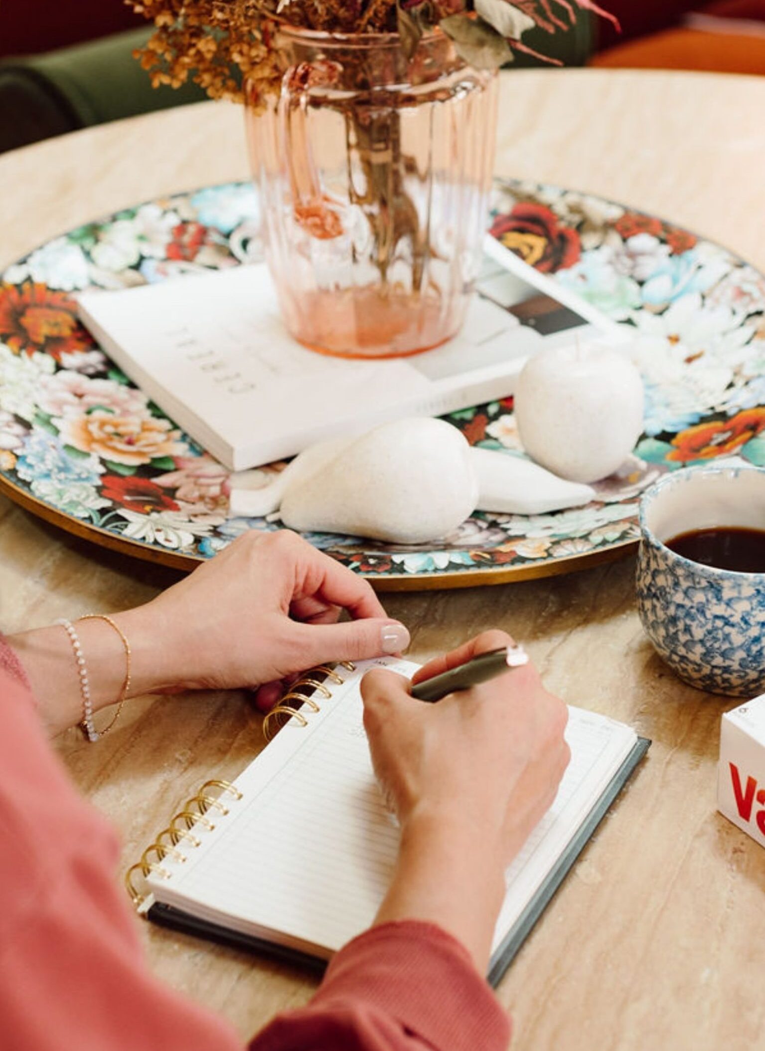 A view over the shoulder of a woman with a pen and notepad, about to do some journaling at a kitchen table. 