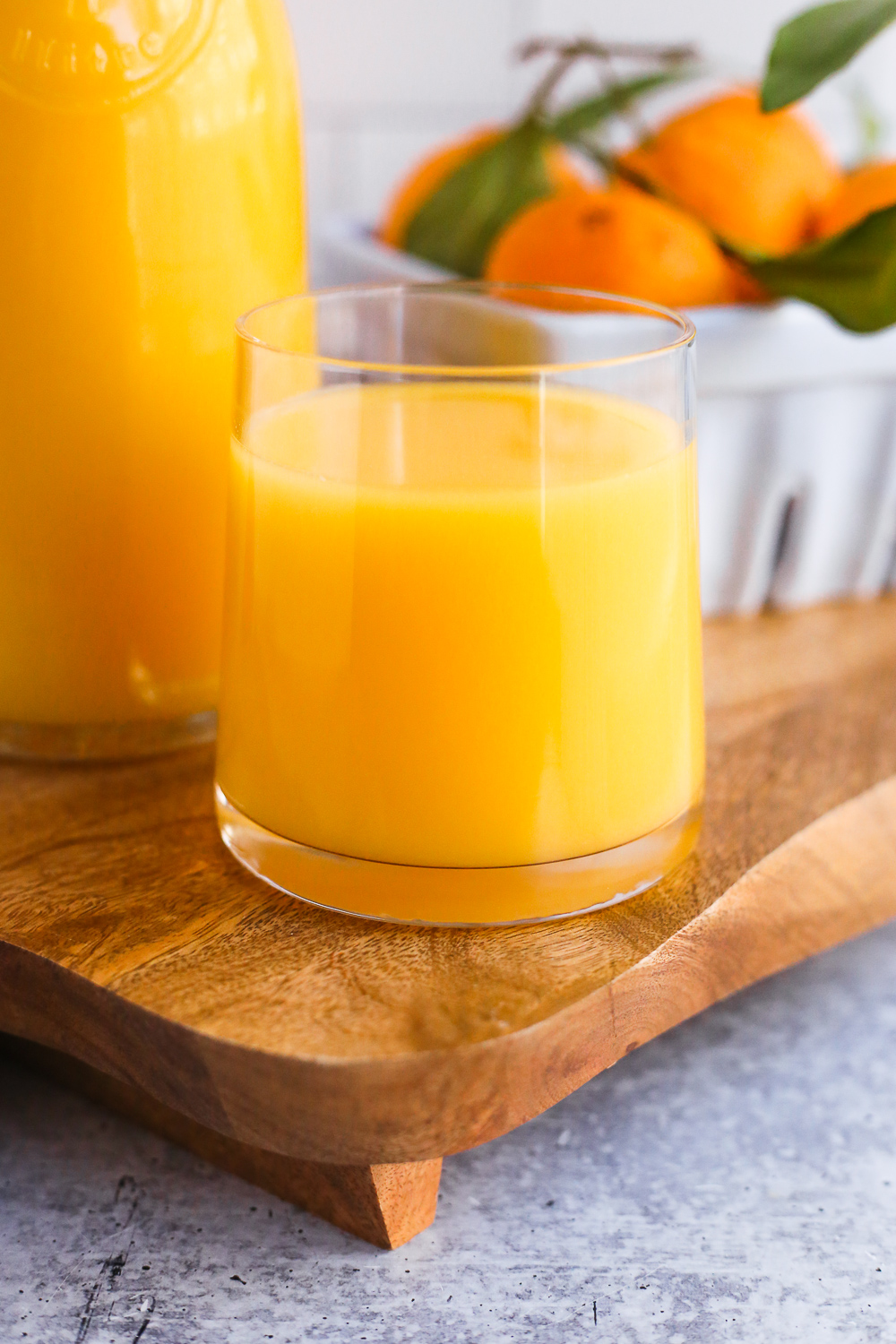 A close up shot of a small glass full of Florida orange juice, with a carafe of orange juice and fresh oranges in the background