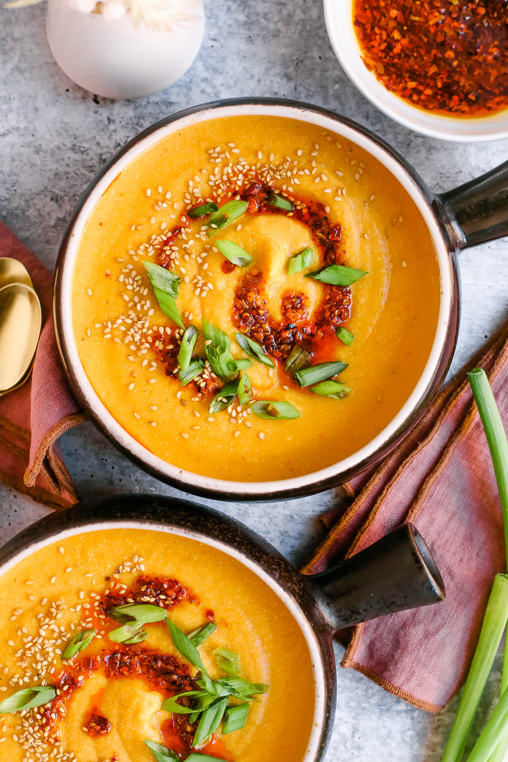 Close shot of the slow cooker miso butternut squash soup, served in black ceramic bowls with a short handle and garnished with chili oil, green onions, and sesame seeds