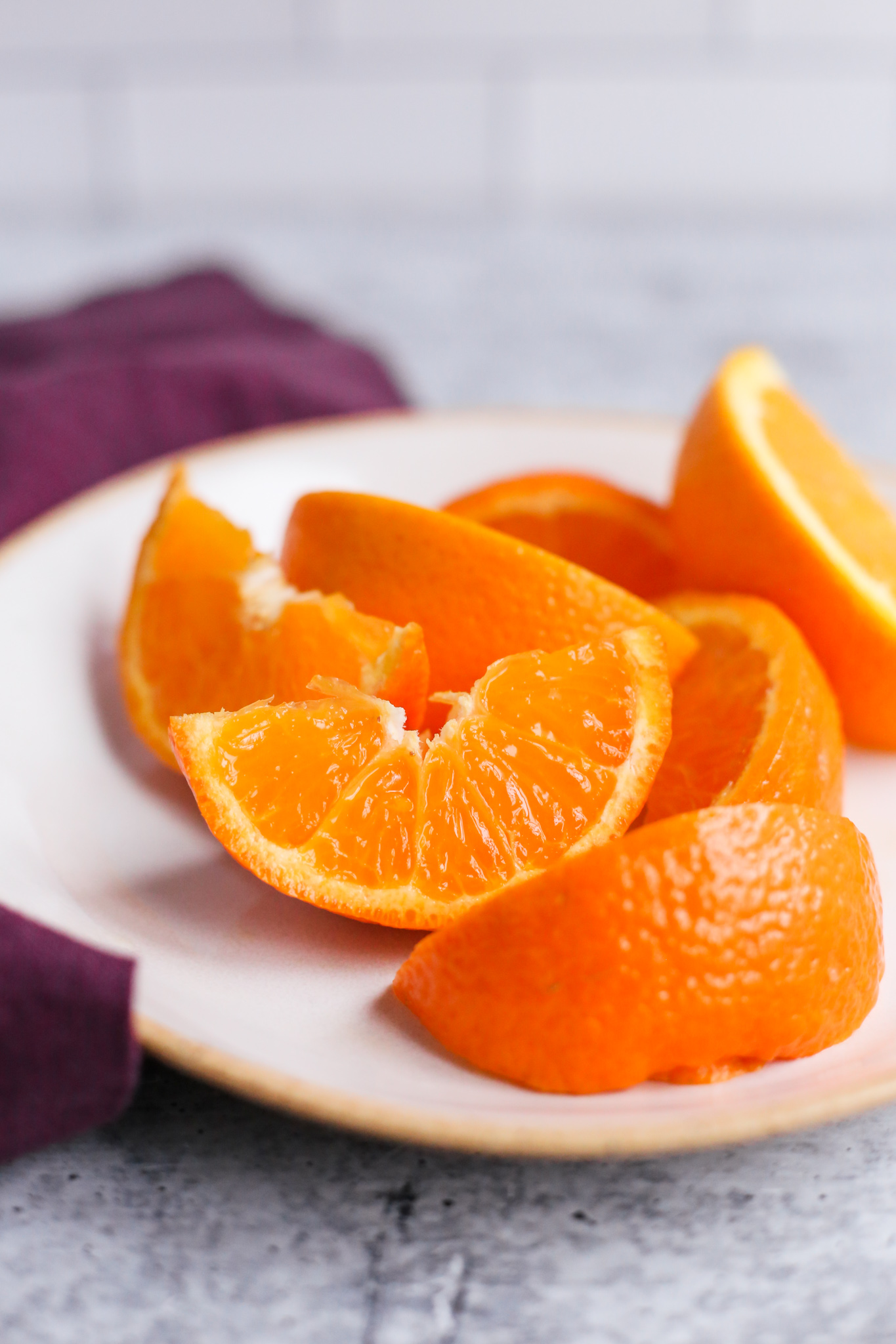 Vertical image of vibrant orange slices of Florida Oranges on a beige ceramic plate