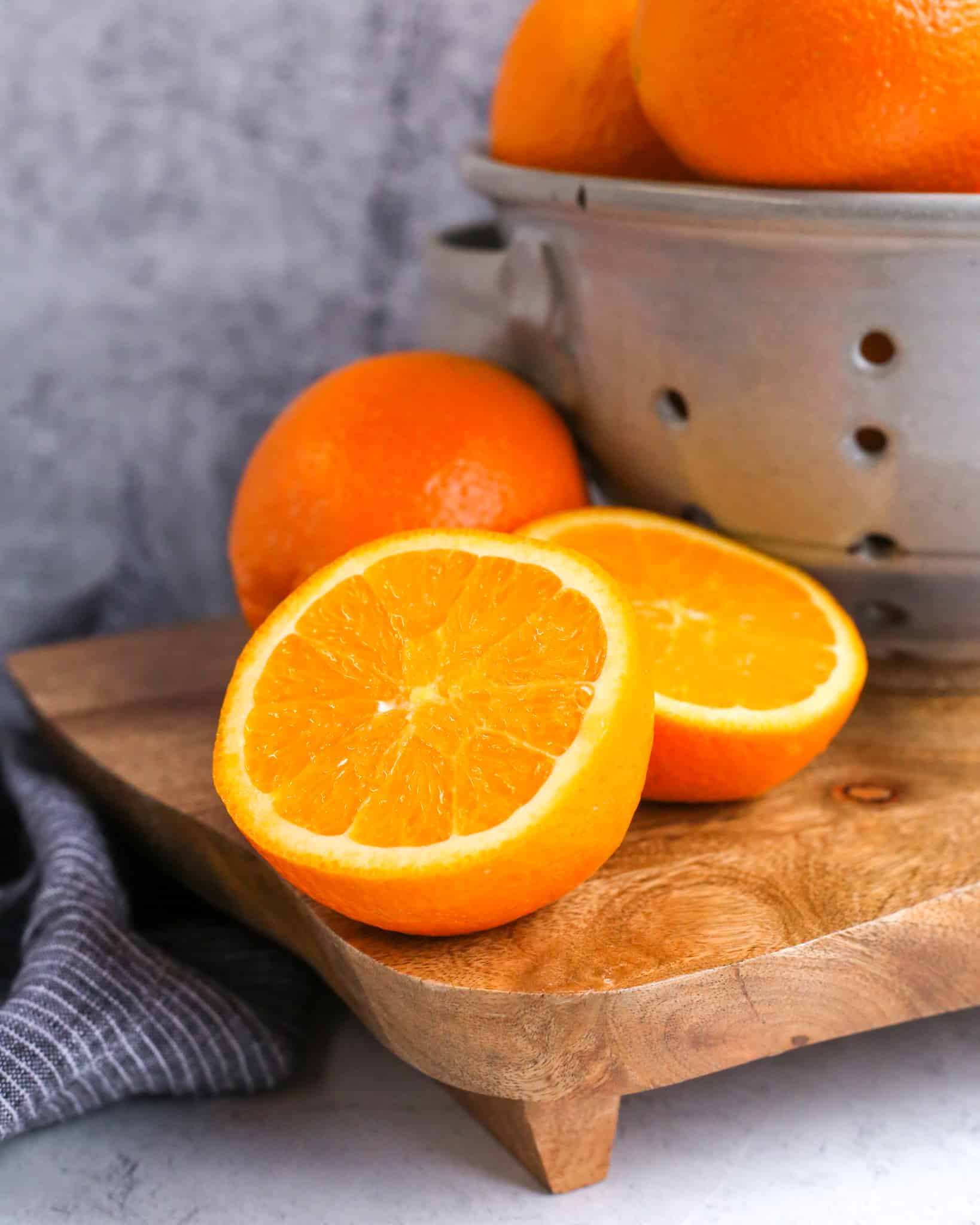 A vibrant, juicy Florida orange is cut in half and placed on a cutting board in front of intact Florida Oranges on a grey stone kitchen counter