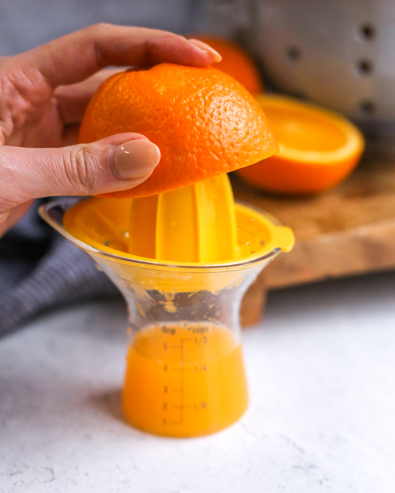 A woman's hand squeezes half of an orange over a citrus juicer, which is collecting fresh squeezed Florida orange juice for the recipe