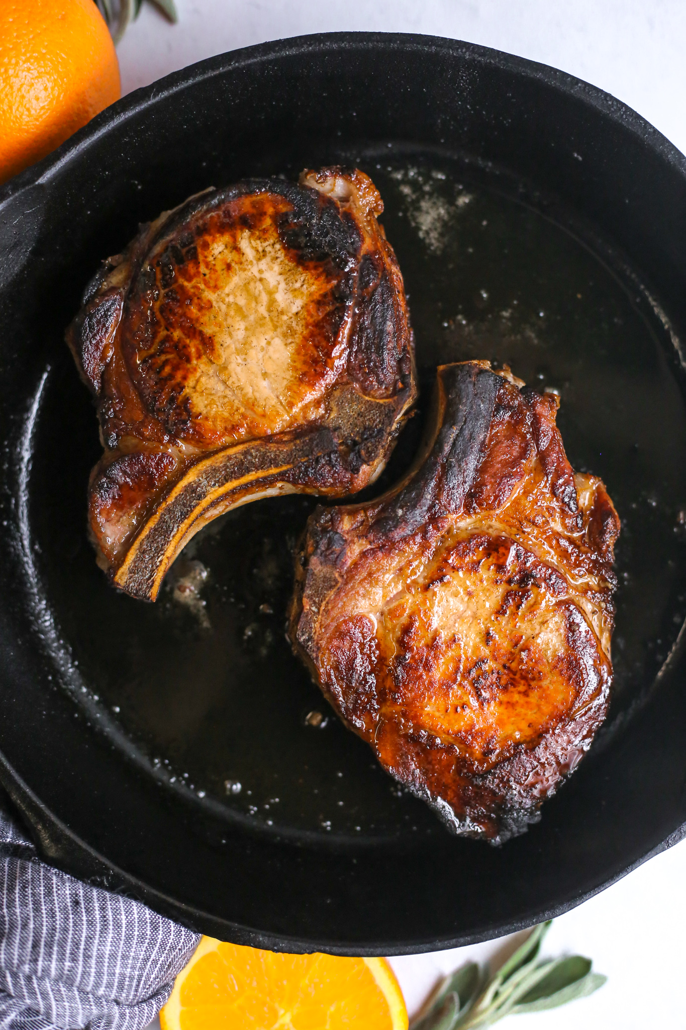 Overhead shot of pan seared, thick cut, bone in pork chops that have been brined with Florida orange juice, cooking in a cast iron pan and charred around the edges