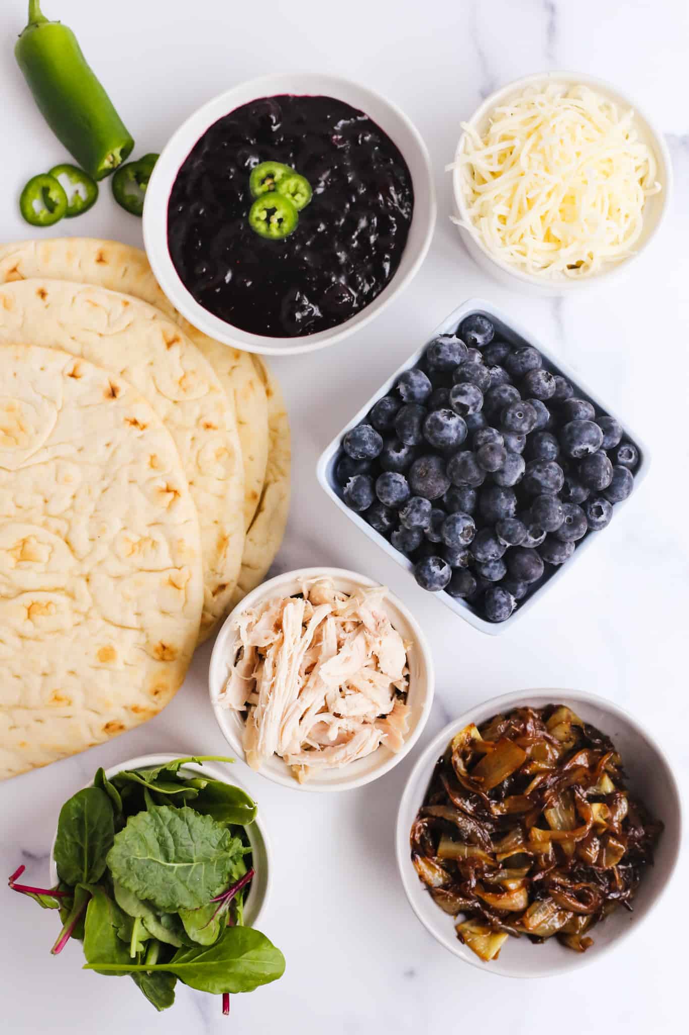 Overhead view of the ingredients for chicken flatbreads with blueberry balsamic sauce, with additional garnishes for chicken flatbread ideas for summer