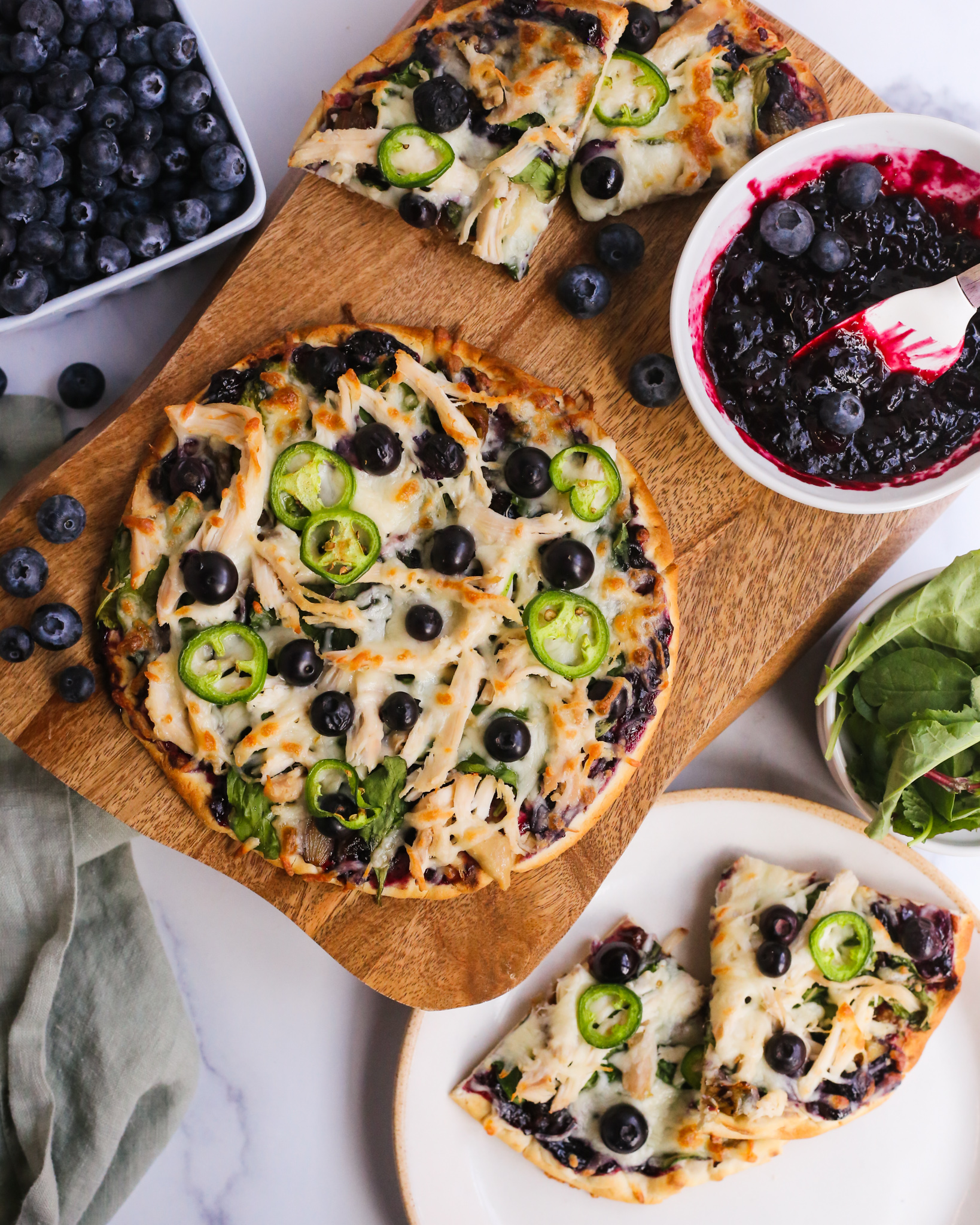 Overhead view of a chicken flatbread with blueberry balsamic sauce for summer, served on a wooden board with additional fresh blueberries