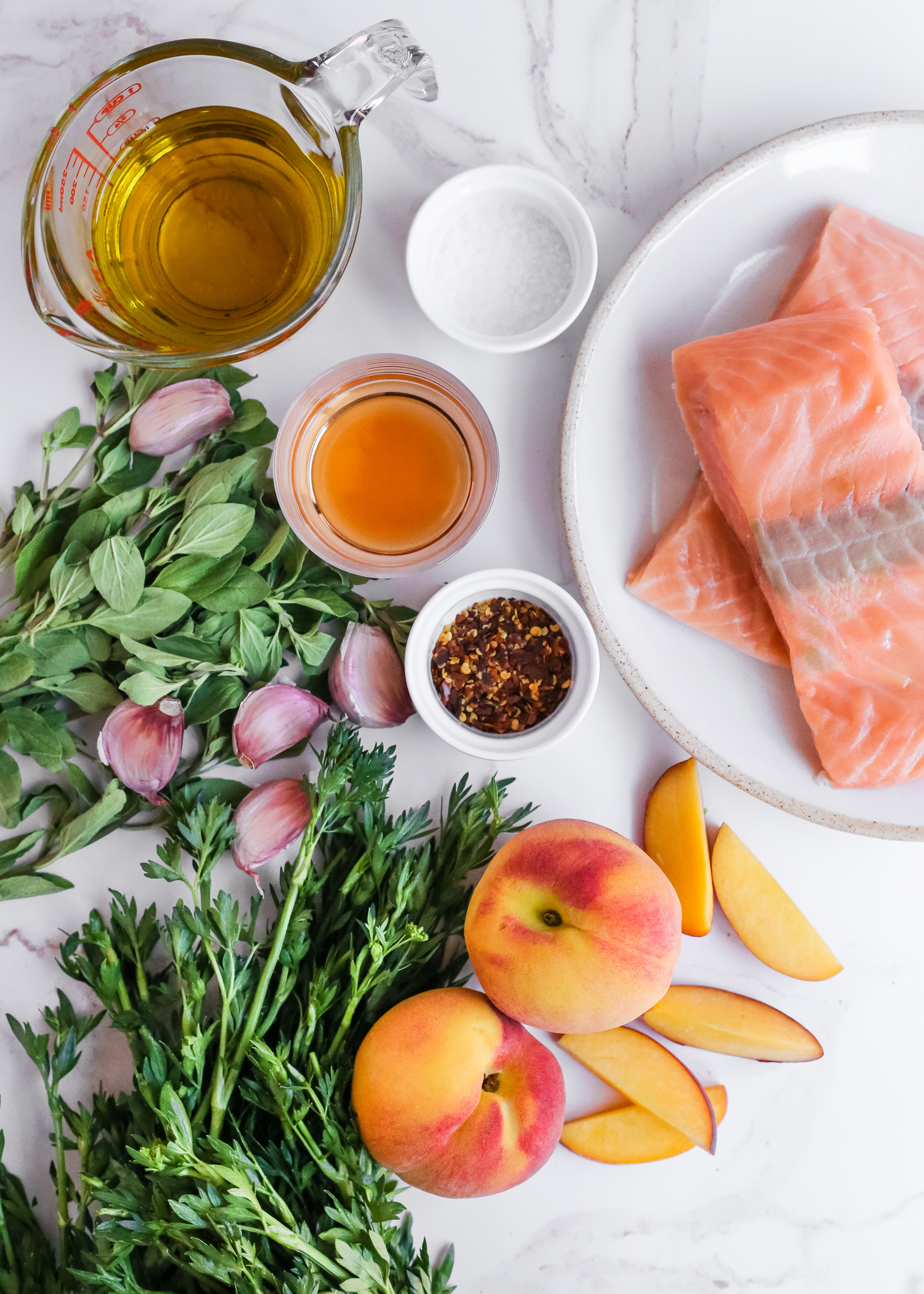 A collection of ingredients for a summer salmon salad recipe, including salmon fillets, parsley, oregano, garlic, peaches, olive oil, red wine vinegar, and salt