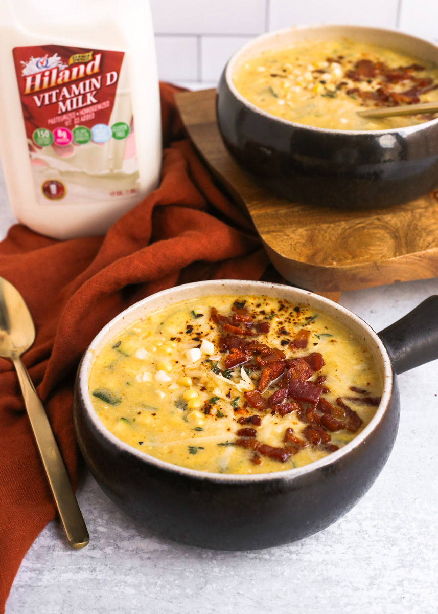 Two bowls of corn chowder with summer vegetables and bacon, served with Hiland Dairy whole milk
